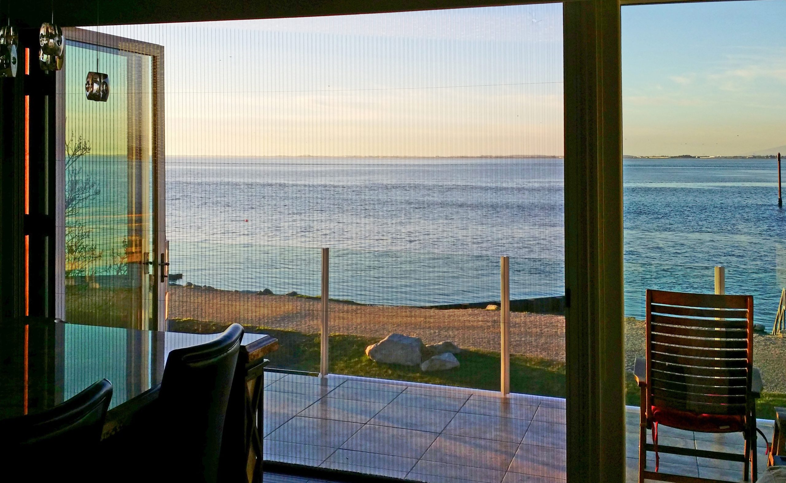 Retractable pleated screen pulled open on a folding glass wall overlooking the water